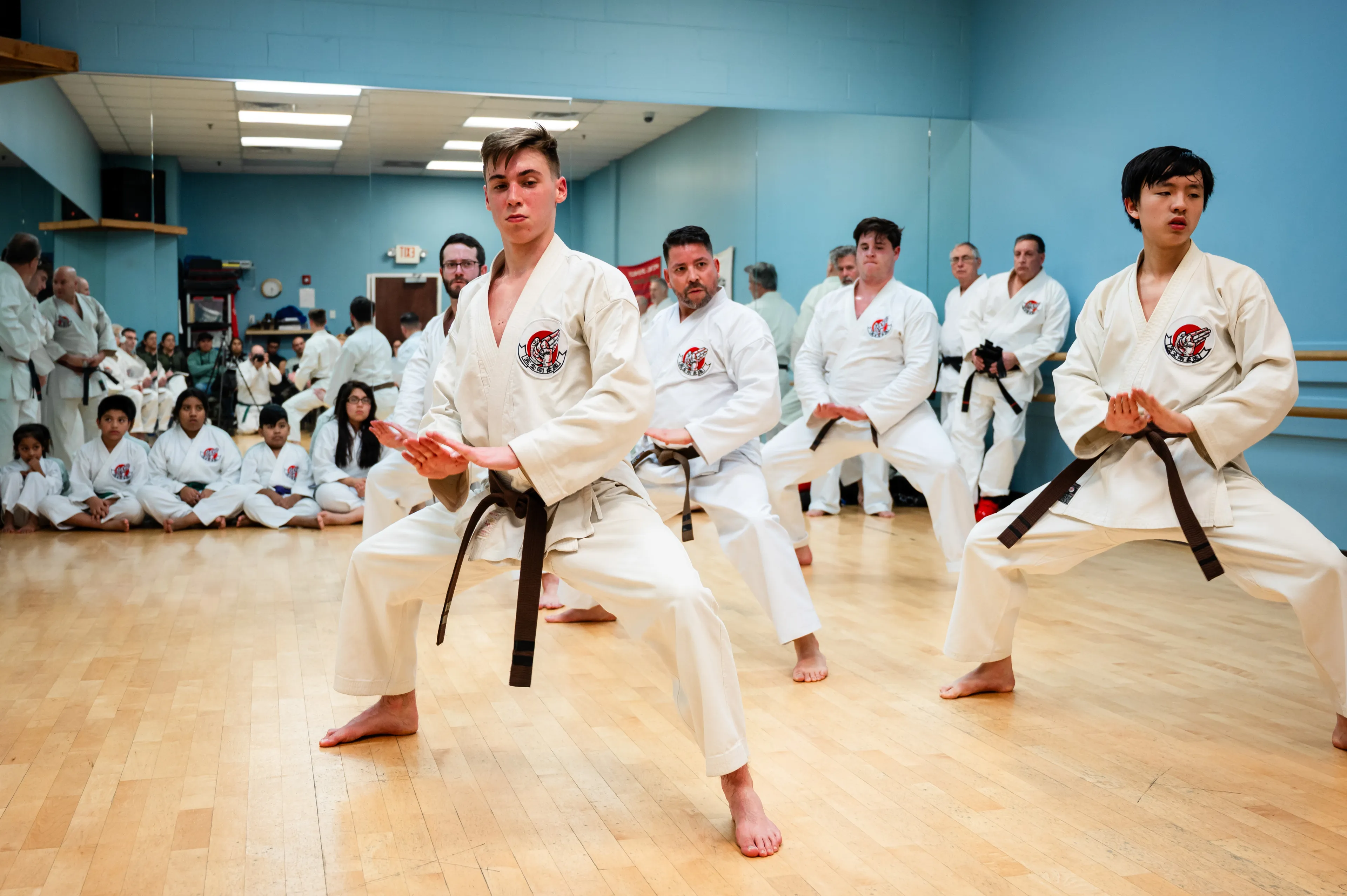 Adult and teenage Kanzen Goju-Ryu students holding the same stance in unison while younger children watch from the mat at the Marlboro dojo